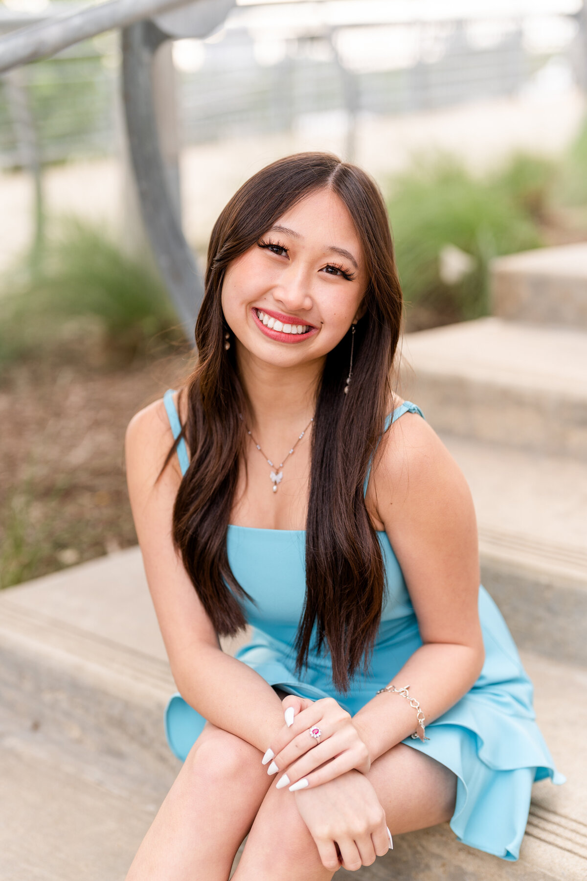 Houston High School senior girl sitting on steps and leaning on knees while smiling and wearing baby blue dress in Downtown Houston