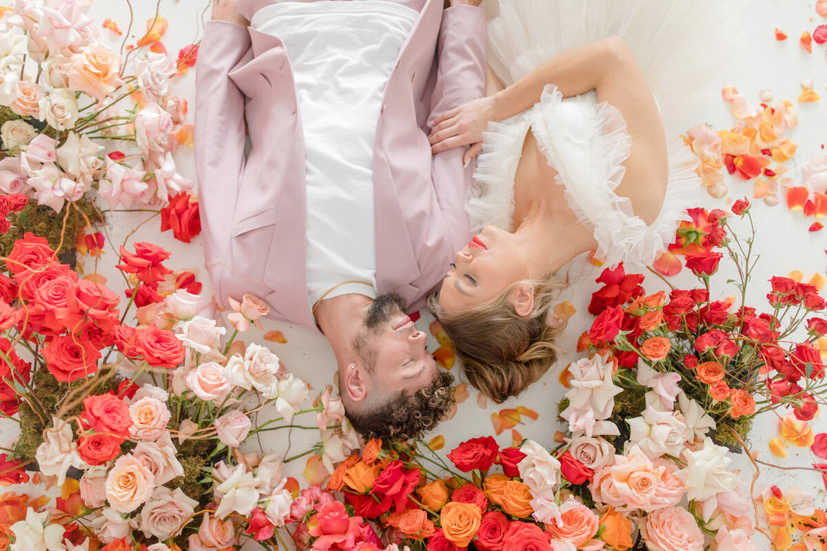 bride and groom laying down  surrounded by bright  florals and decor for a bold and bright wedding at Supply Manheim in Lancaster