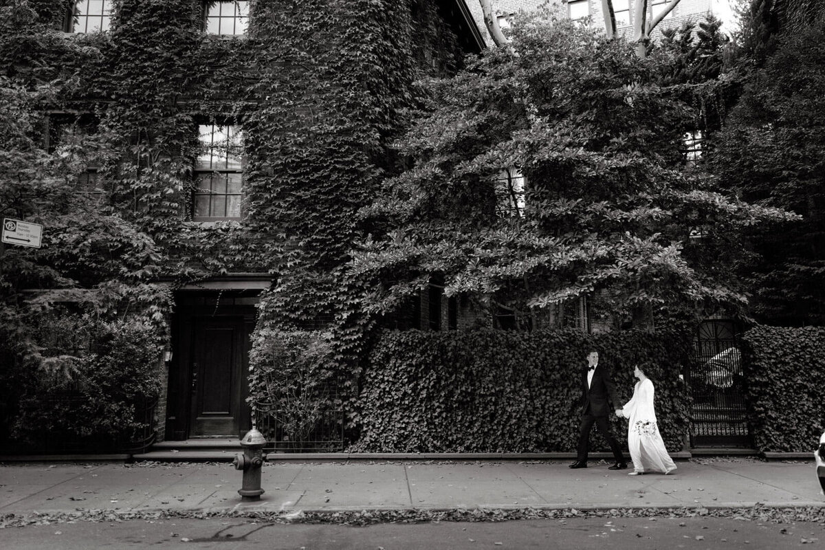The bride and the groom are walking along the sidewalk, showing a grass-covered wall and building in New York City.