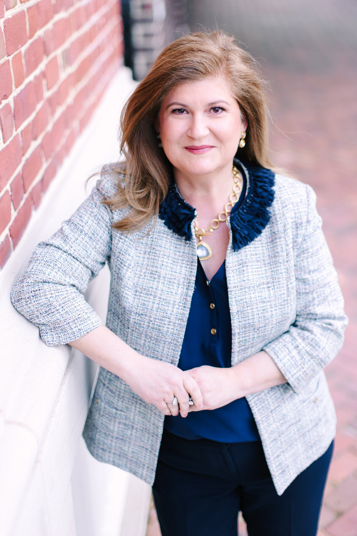 Woman in smart blue outfit leaning against a red brick wall