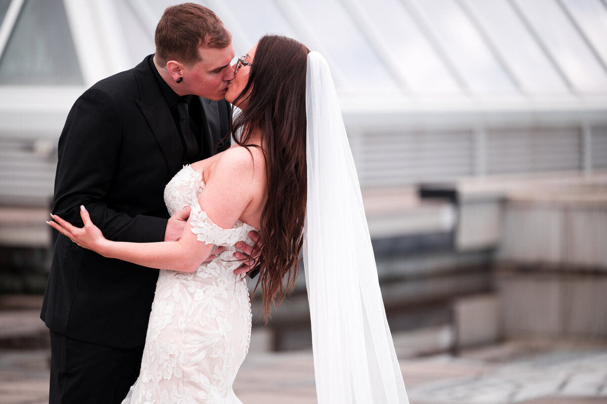 close up of bride and groom kissing, brides veil blowing in the wind