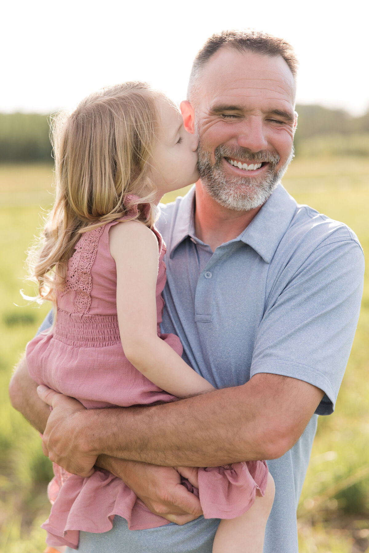 A father is holding his little girl and she is kissing his cheek