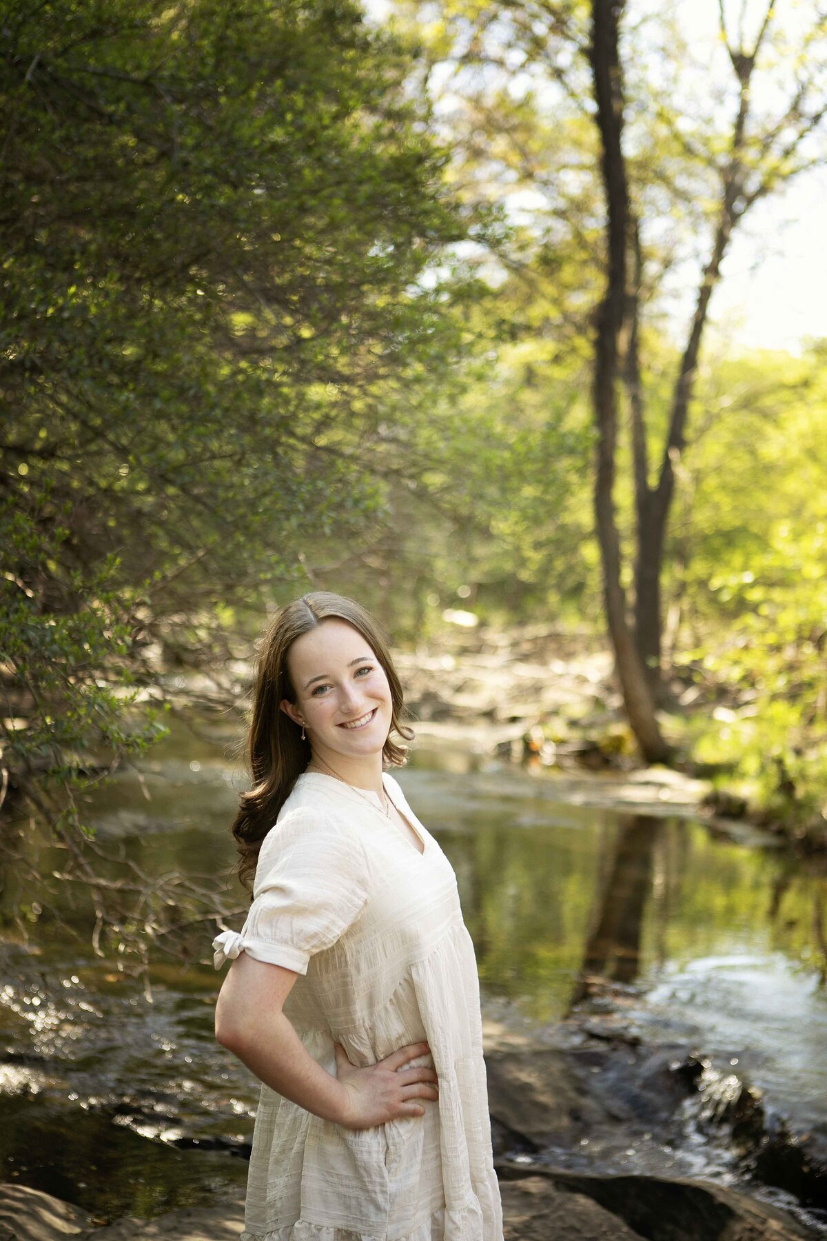 Older sister standing on a rock in the creek in Flower Mound, looking serene and relaxed while posing for her individual picture