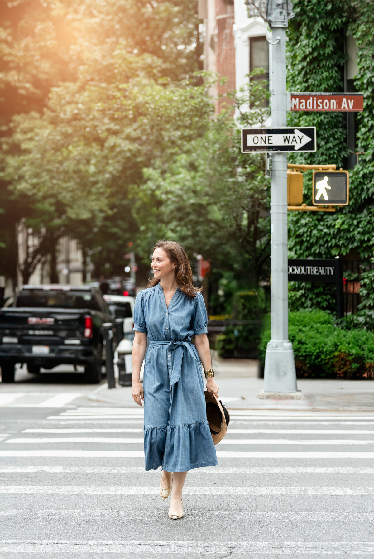 woman walking across road in manhattan madison avenue wearing blue dress and carrying a straw hat