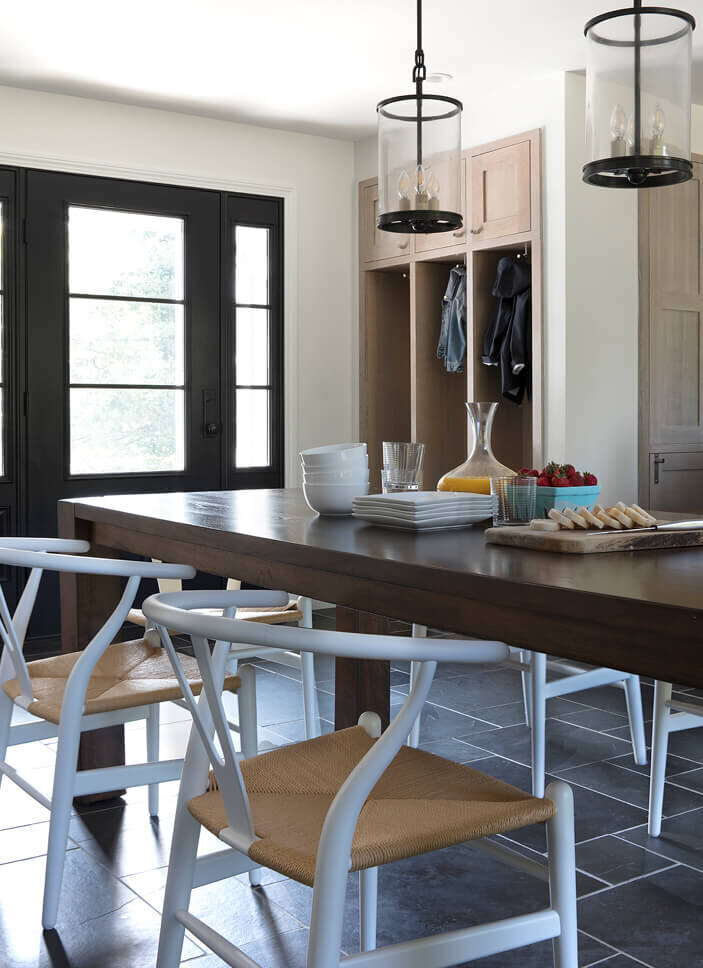 Interior designers in Boston, MA design a dining room with a modern table, slate flooring, Ralph Lauren pendants, and a view of new doors and mudroom cabinets.