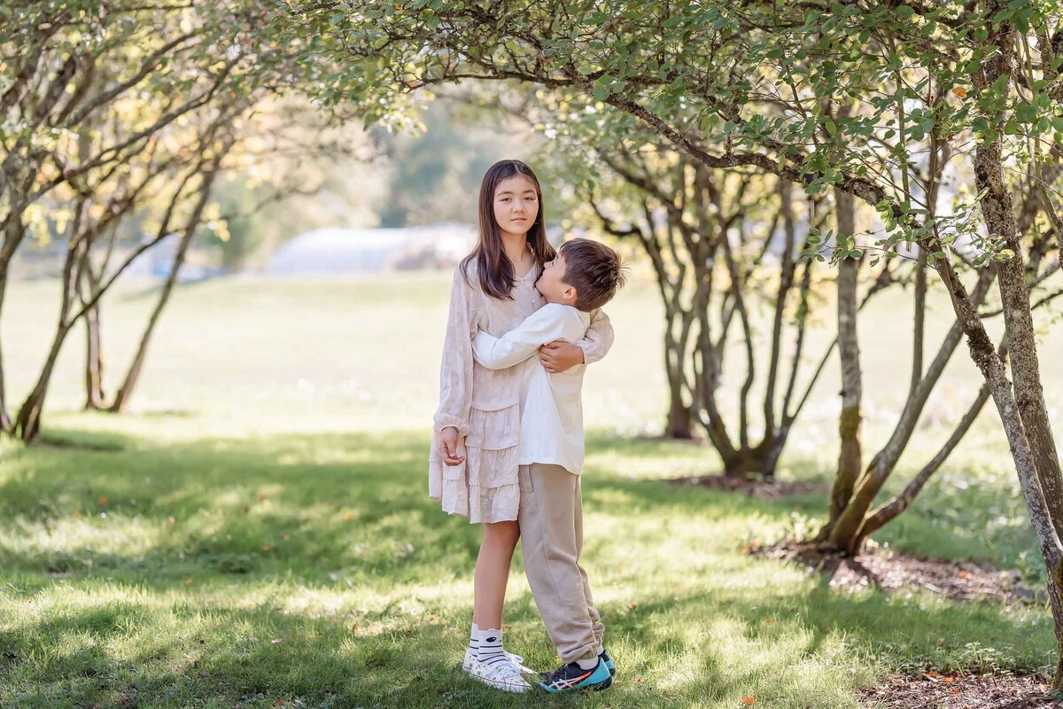 Big brother hugging his little sister in a Seattle park, bathed in soft, natural light during a sweet sibling moment.