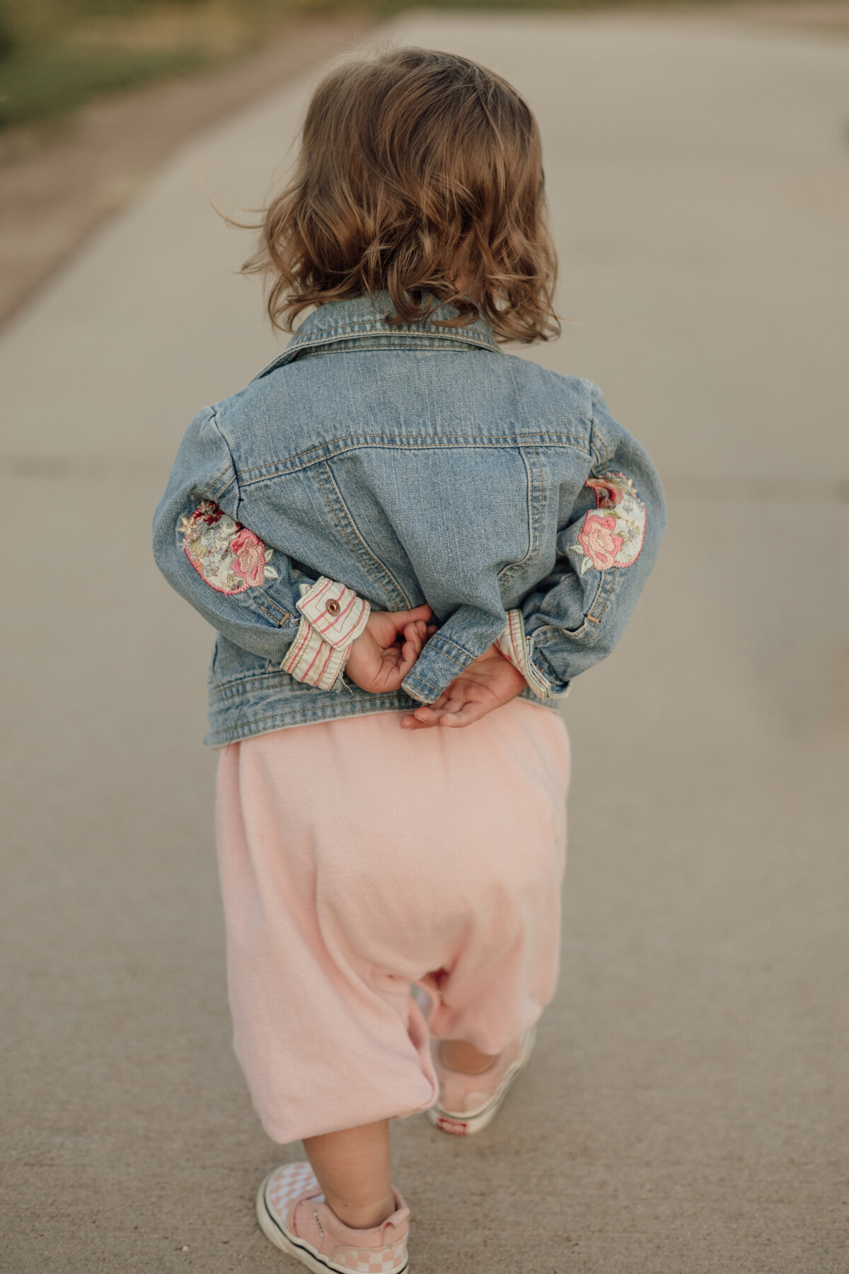 little girl with hands behind her back walking away from camera during lifestyle family session at sandstone ranch in longmont colorado with alexis adkins photography