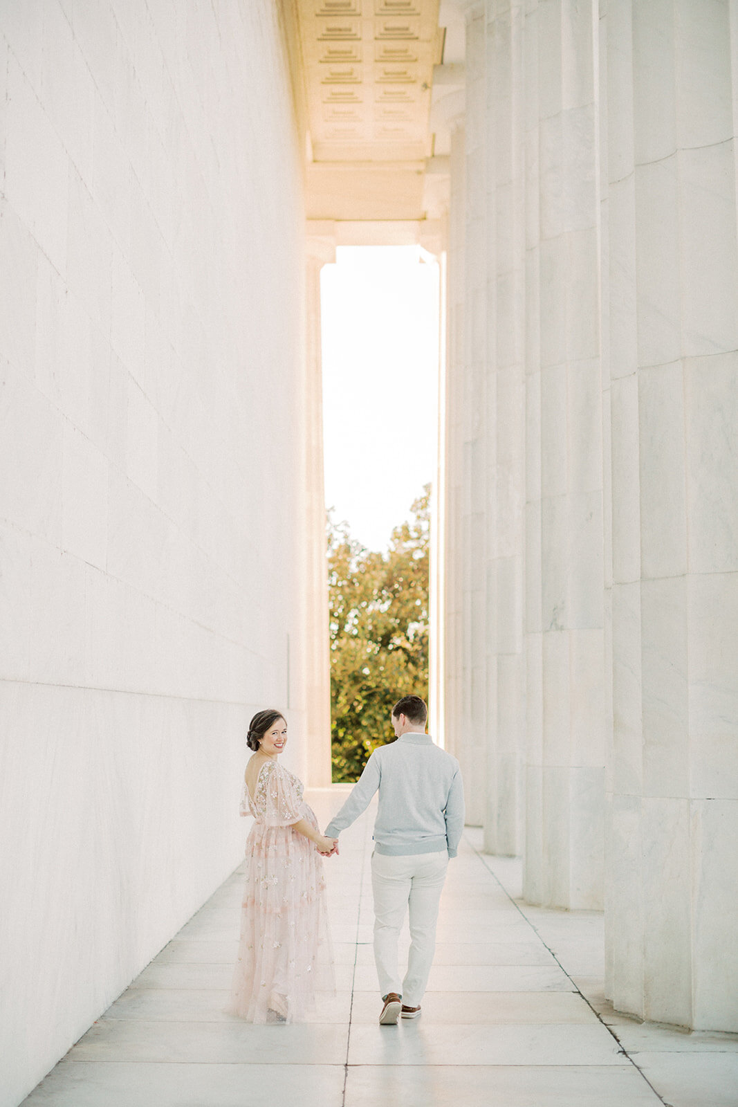 Husband and wife walk together at Lincoln Memorial as wife turns to look back at the camera.