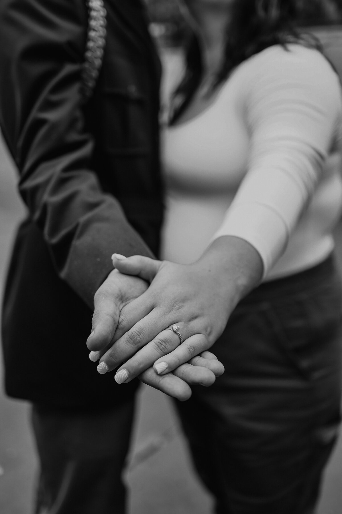 black and white image of man and woman holding hands showing off diamond ring