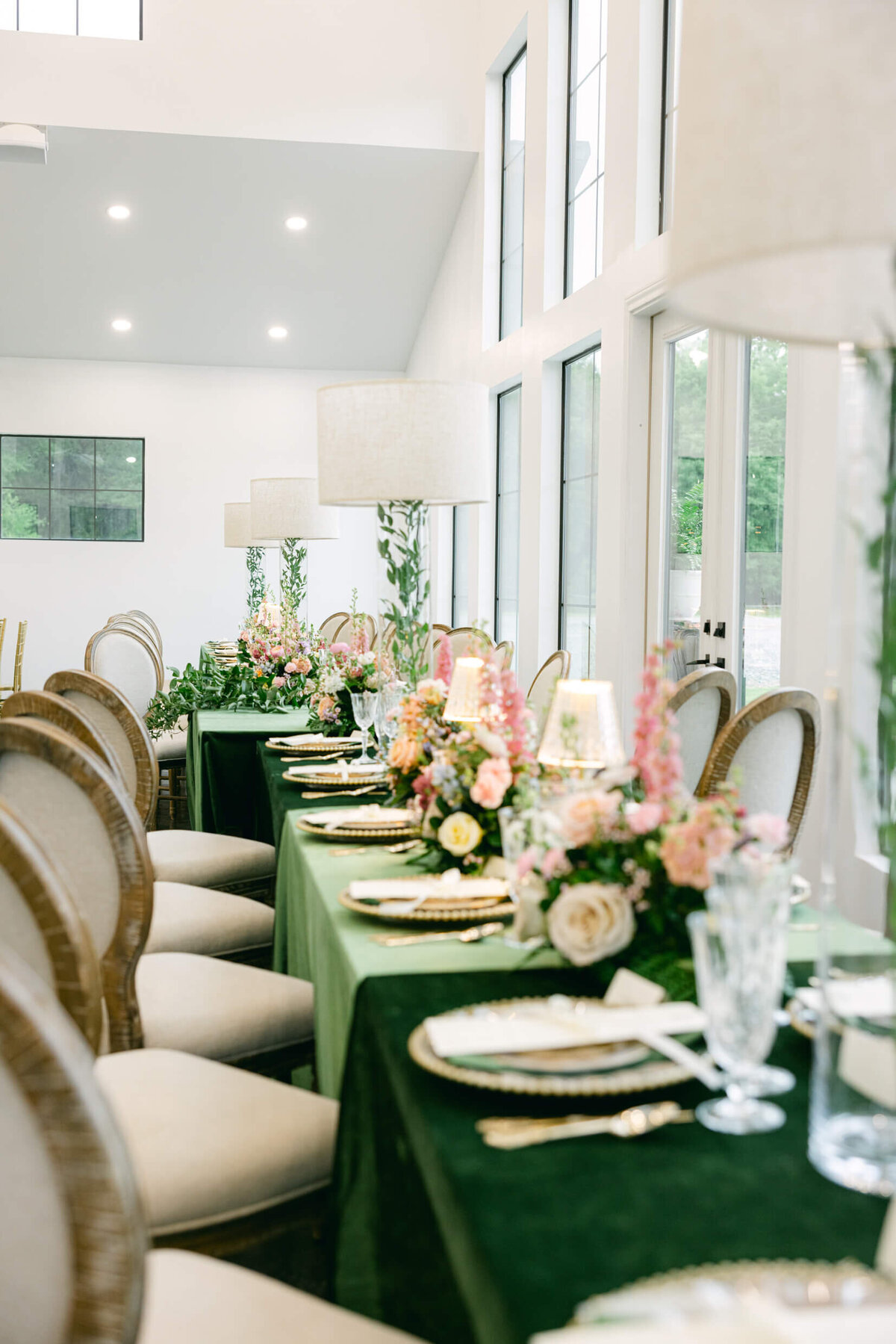 A wedding day photo of the tables in the reception hall that are covered in green linens with florals & candles on top