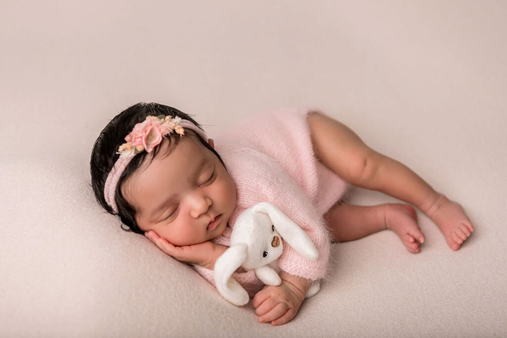 Connecticut newborn photographer specializing in posed newborn portraits captures sleeping baby girl with pink floral headband holding white bunny prop