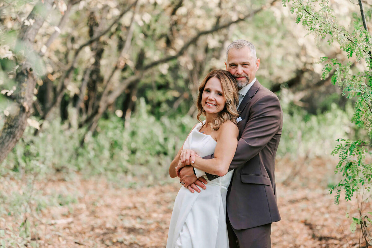 Groom holds bride  close by some fall trees.