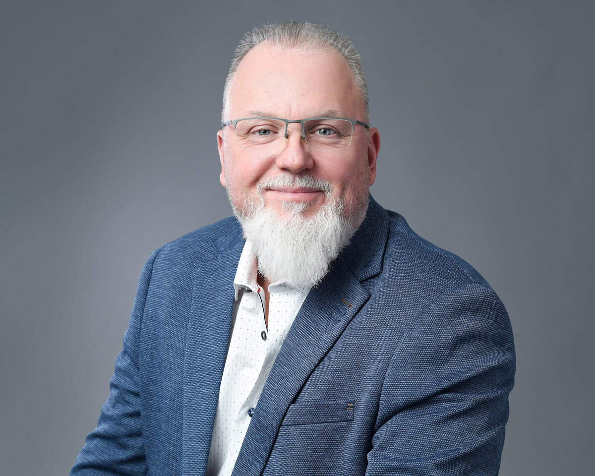 Professional headshot of a distinguished individual in a blue blazer and white shirt, captured against a clean, neutral background. The subject's confident expression conveys approachability and professionalism—ideal for business and branding photography.
