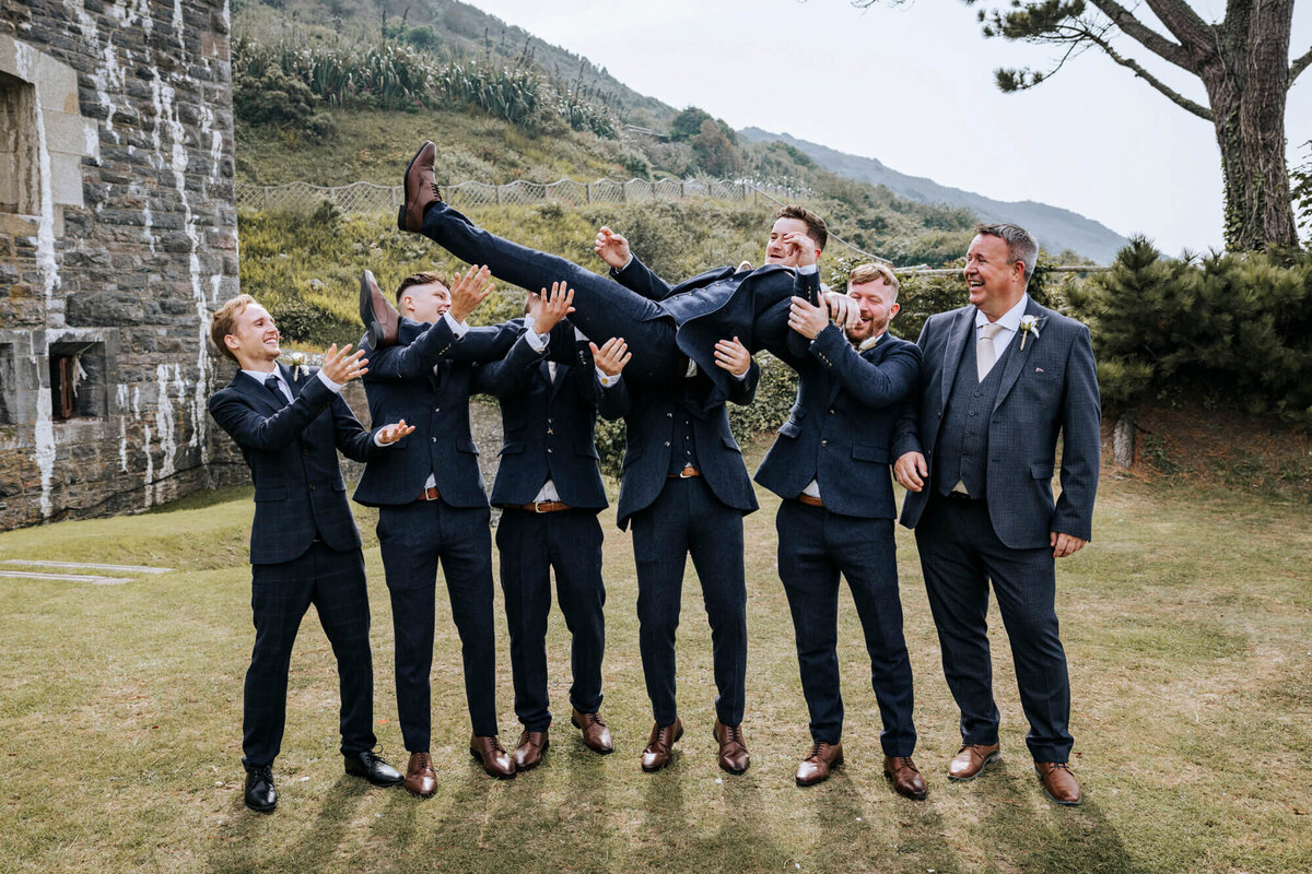 A group photo of the groomsmen holding the groom in the air