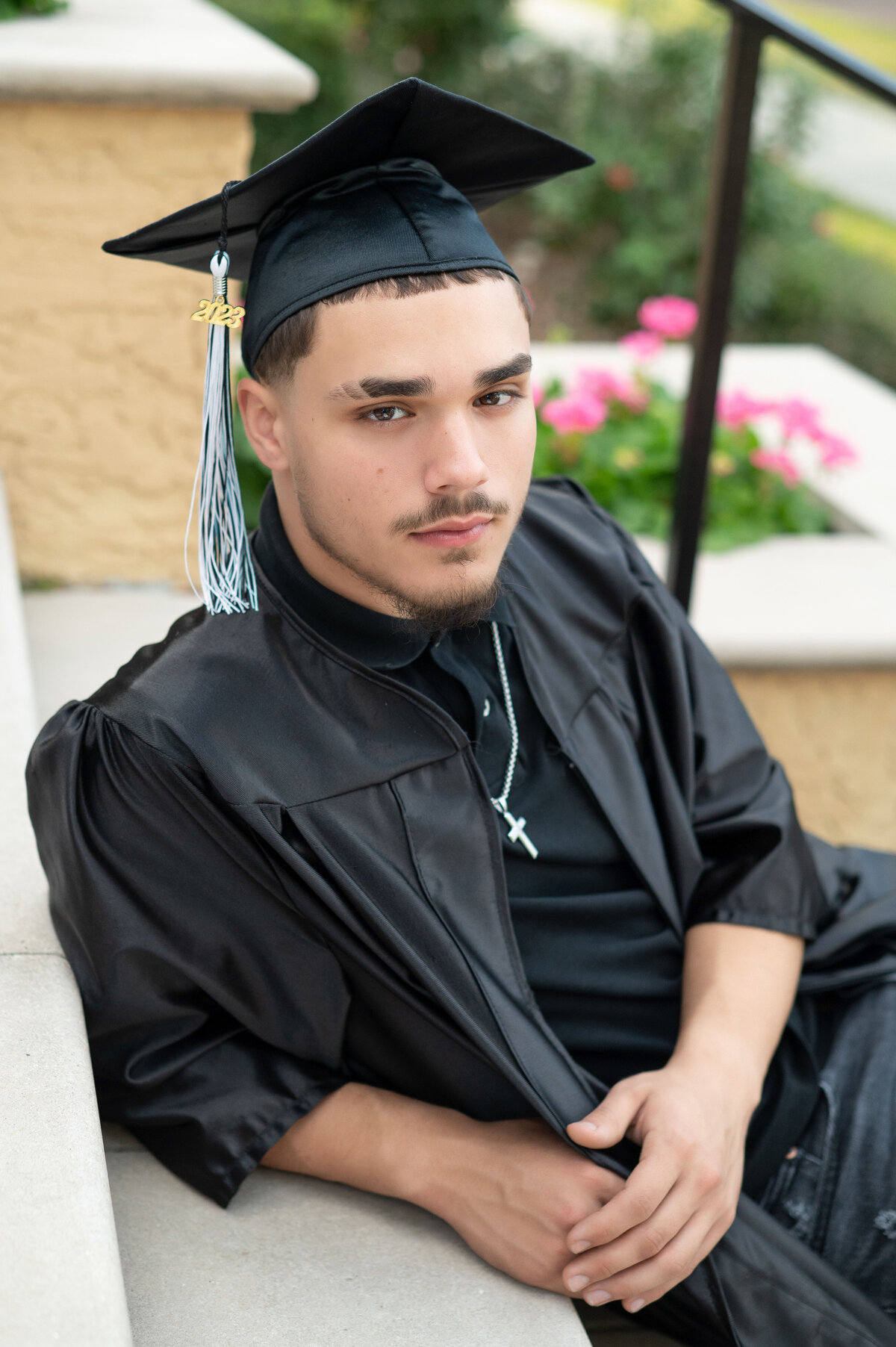 High school senior boy in cap and gown leans on stairs and looks into camera with a serious expression.