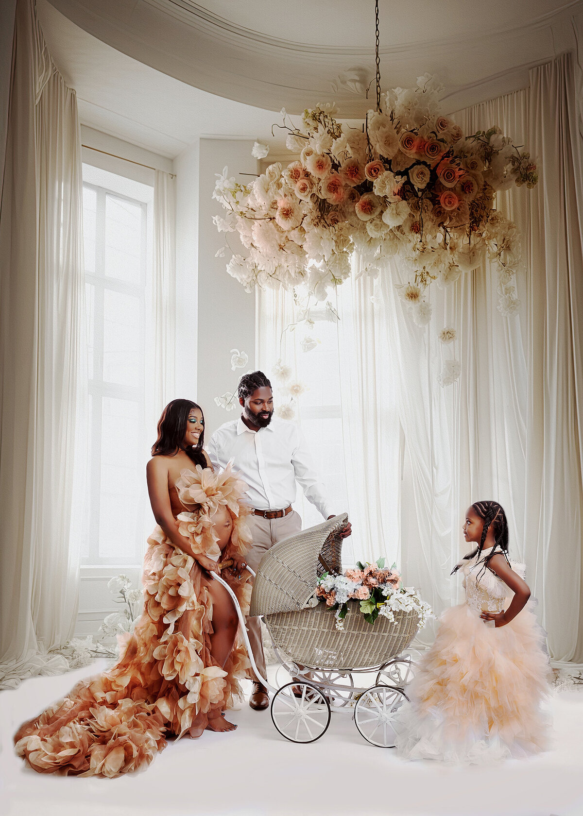 Expecting family portrait with mom and daughter wearing brown and tan gowns and dad in formal attire, posing with vintage pram in a beautiful room background with hanging floral arrangement