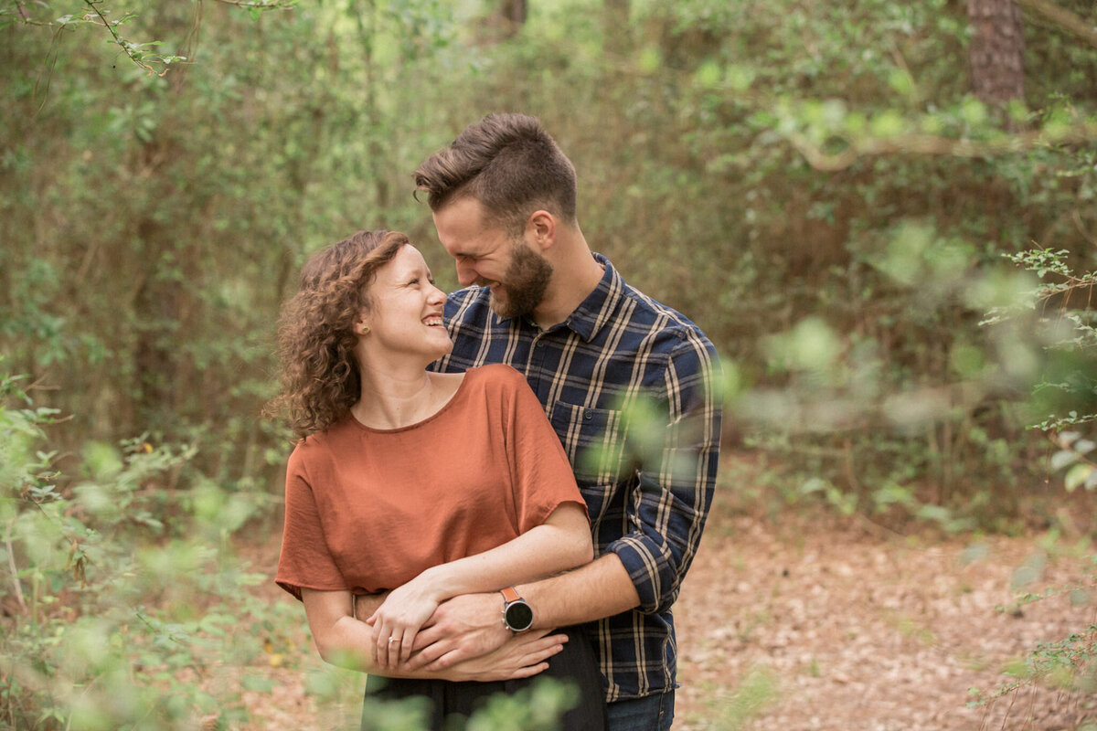 A man wearing plaid wraps his fiancee in a loving embrace  during their engagement photography session.