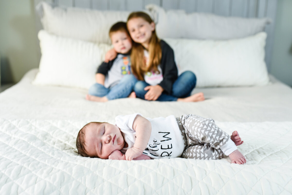 Beautiful lifestyle newborn photography: Newborn boy on a bed with his siblings in background at their home in Mississippi