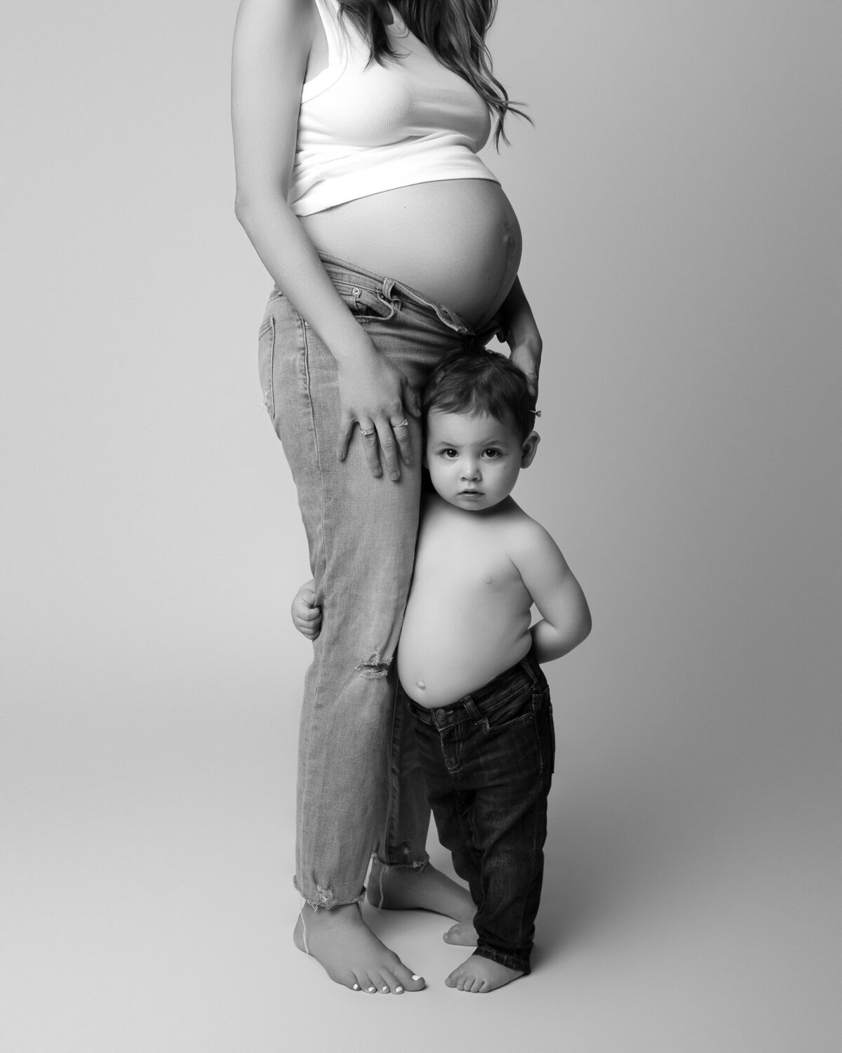 Artistic black and white maternity photo of expectant mother with her toddler pose highlighting pregnancy curves