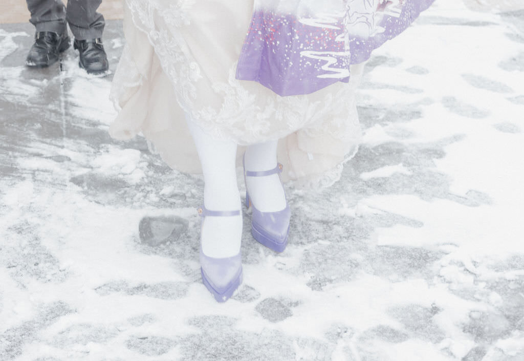 A close up of someone wearing purple heels in the snow.