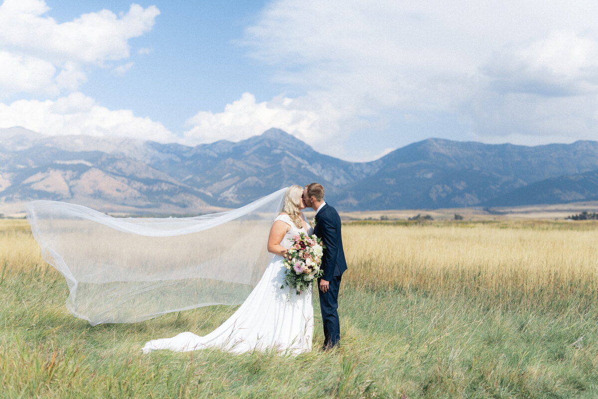 Bride and groom kiss with mountains behind them