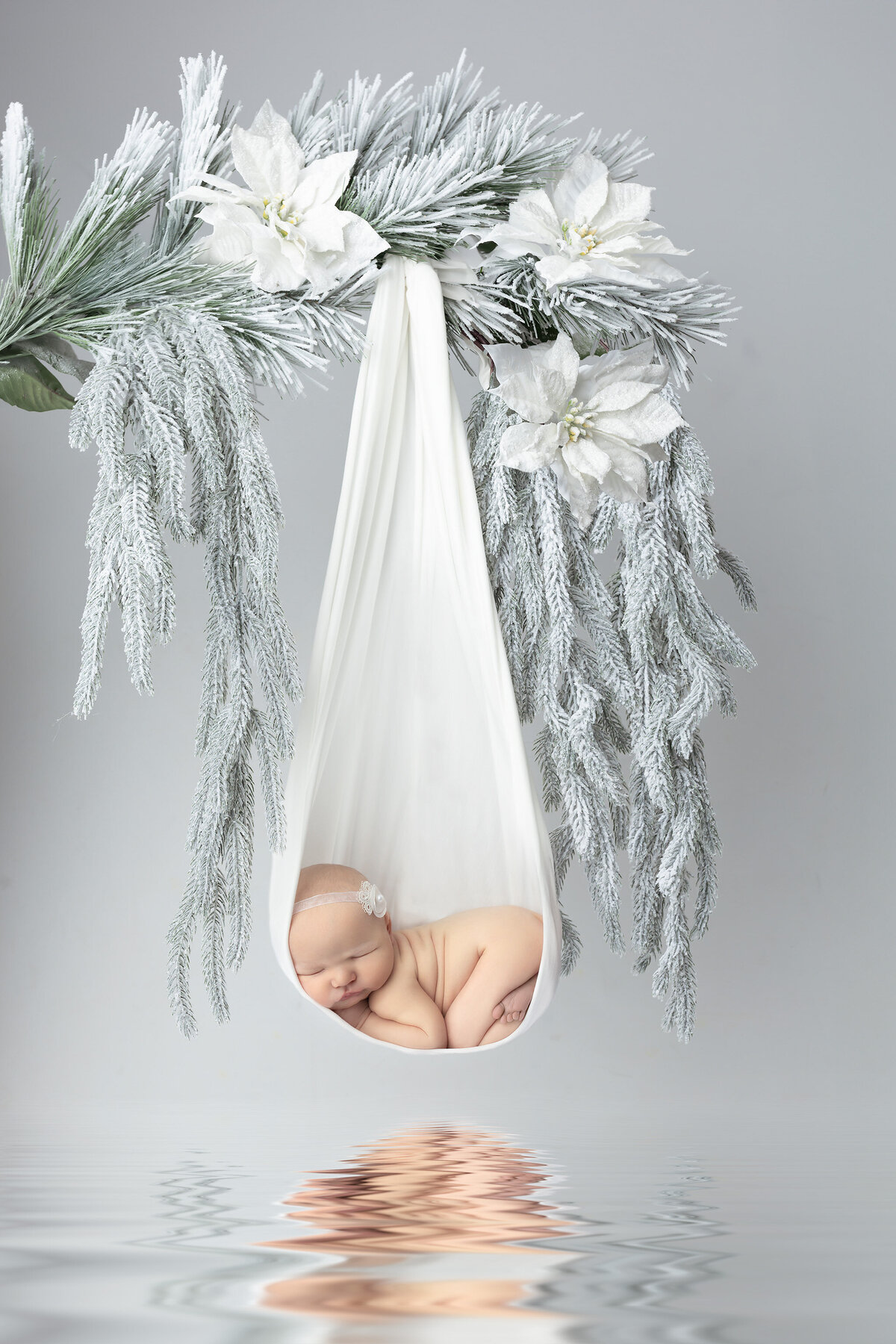 Newborn baby girl peacefully sleeping in a white hanging wrap surrounded by frosted winter greenery, styled by Dallas Newborn Photographer known for dreamy newborn pictures.