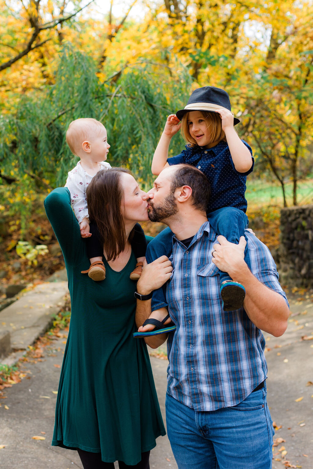 Two parents kiss with their kids on their shoulders.