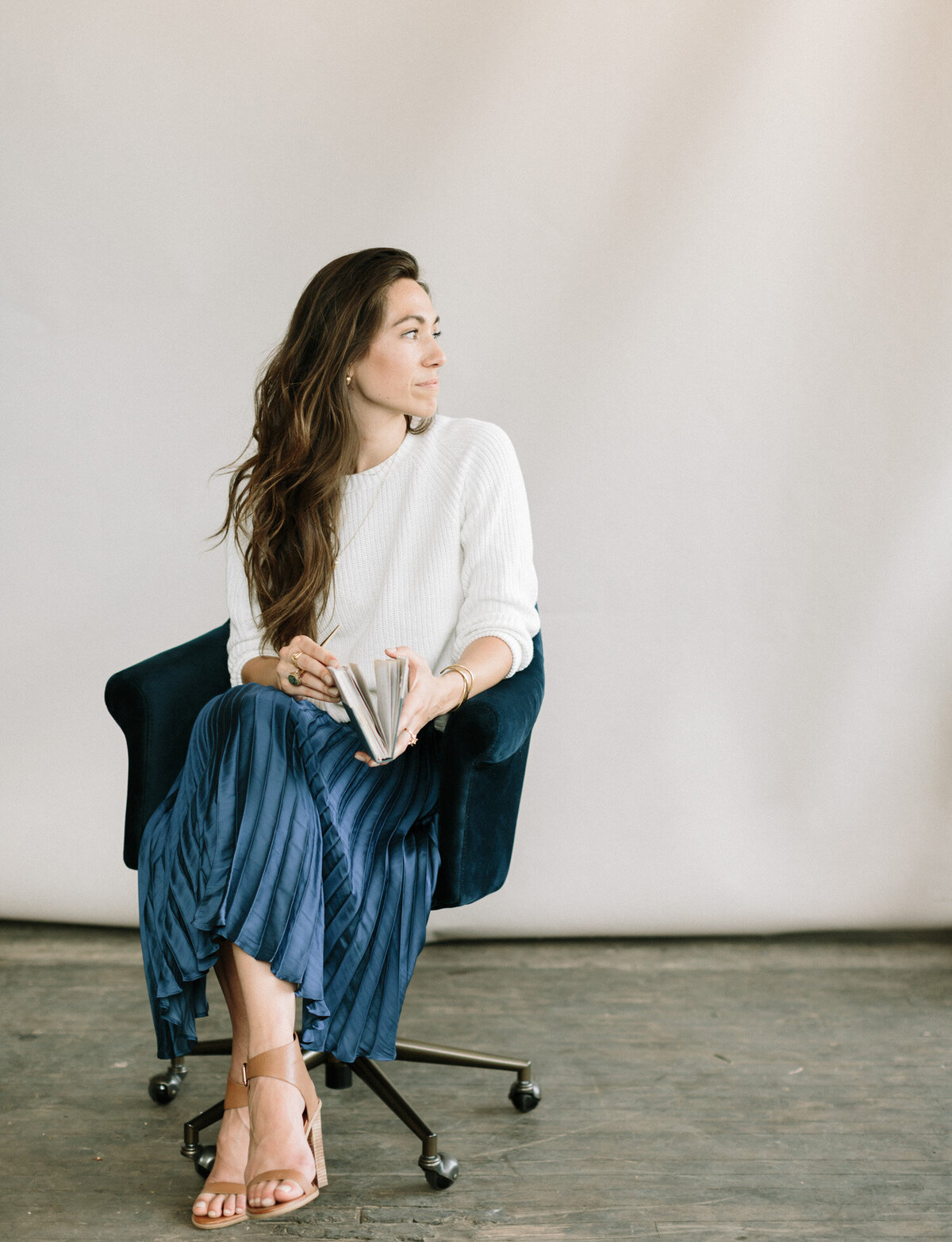 woman in cream sweater, blue pleated skirt in chair with journal for her brand photoshoot