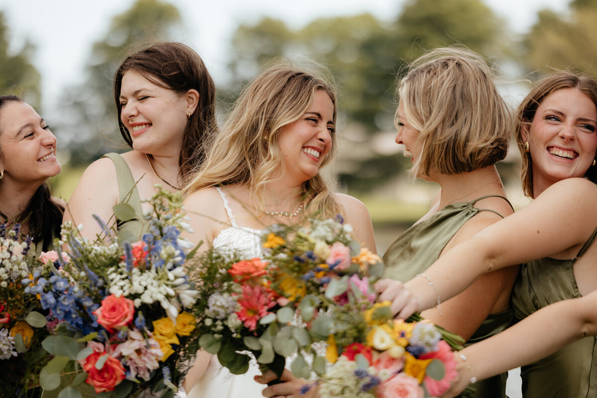 A bride and her bridesmaids smiling at each other with their bouquets at Whitehall Columbia.