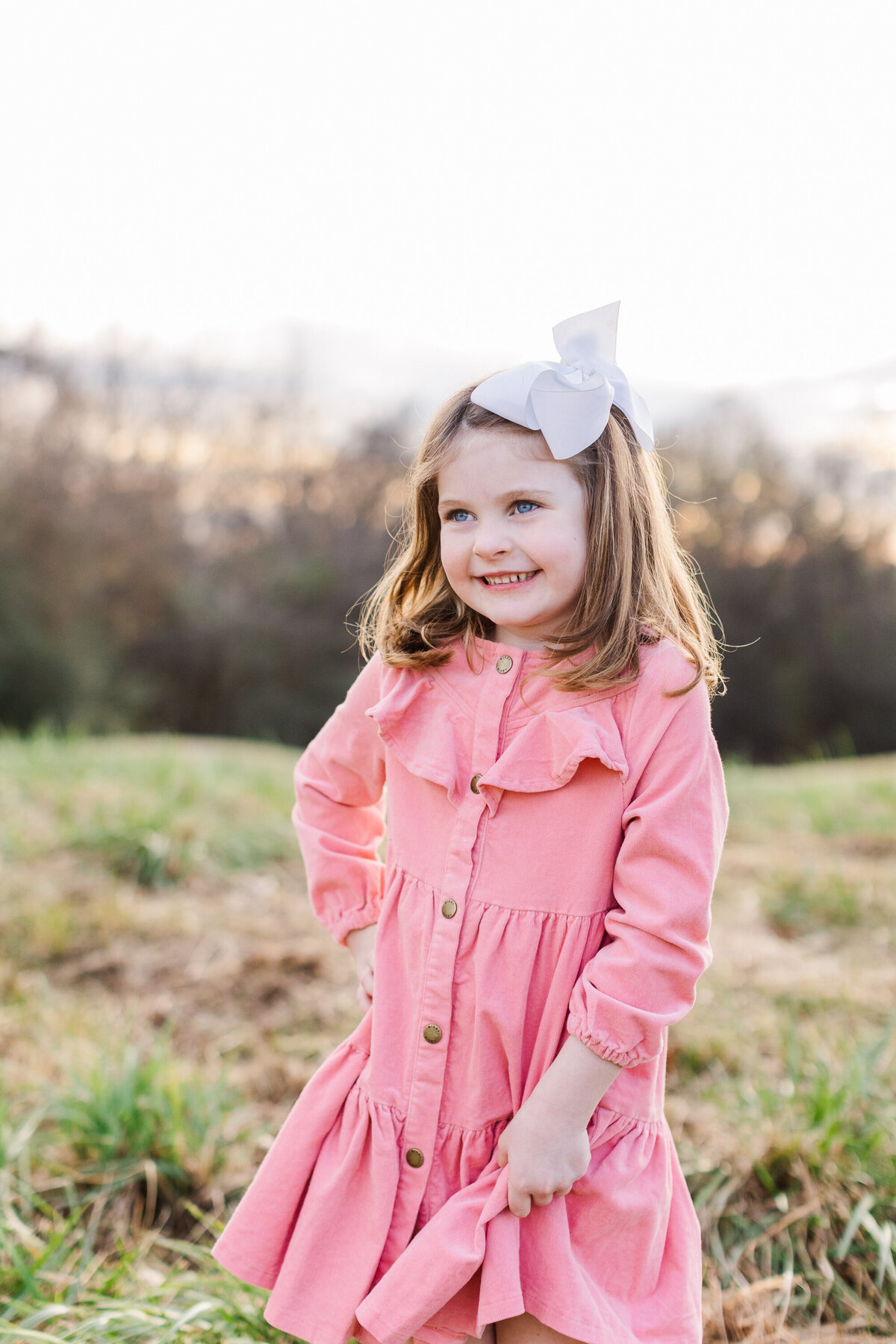 little girl wearing a pink dress smiling in a field