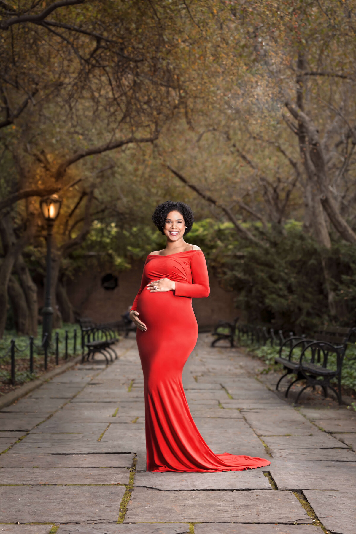 pregnant woman in a red maternity gown standing in a park on a stone path in an outdoor maternity session