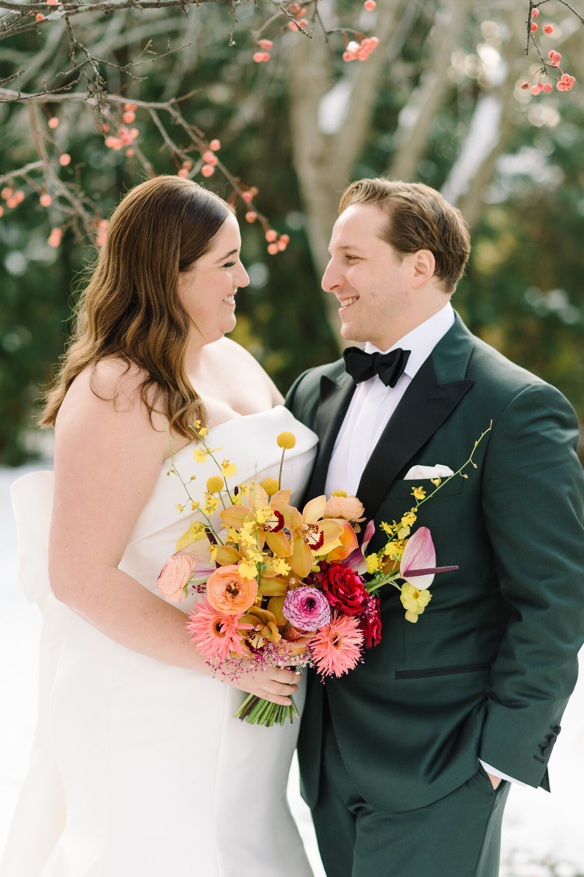 A couple in wedding attire gaze at each other, the bride holds a modern, colourful bouquet.