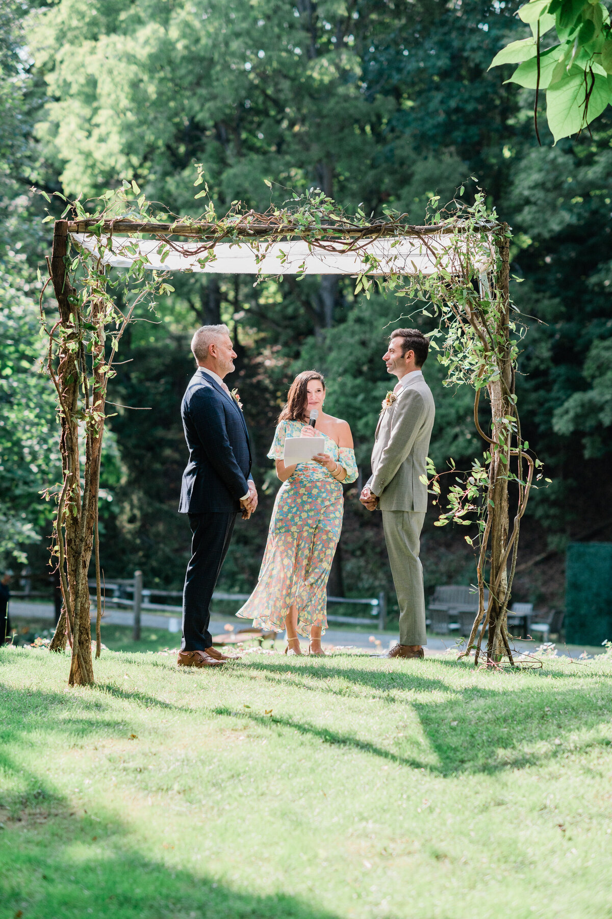 Female officiant speaks as the grooms look at each other 