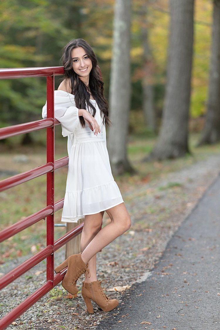 High school senior girl leaning against red gate in woods