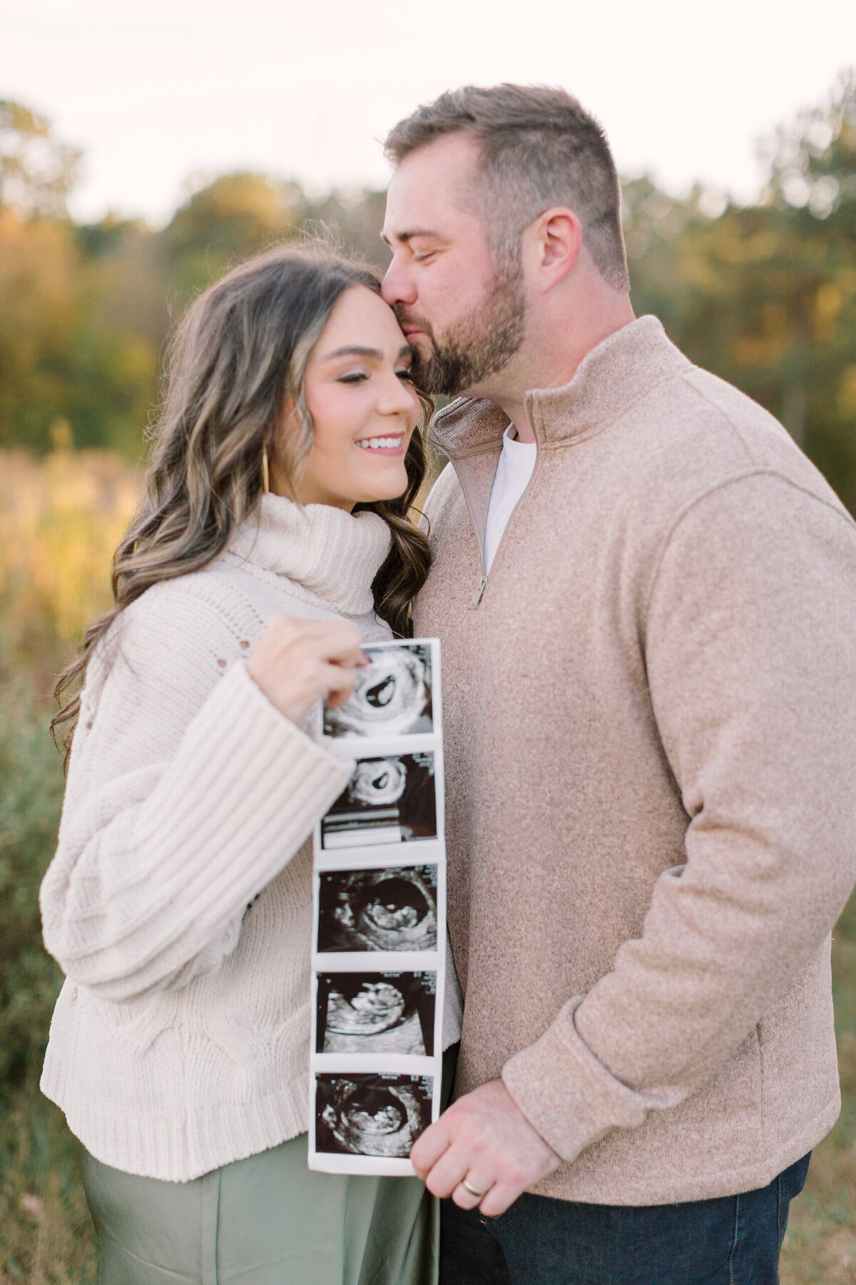 A couple holding ultrasound photos during their maternity announcement session at sunset — Portrait photography in Raleigh.