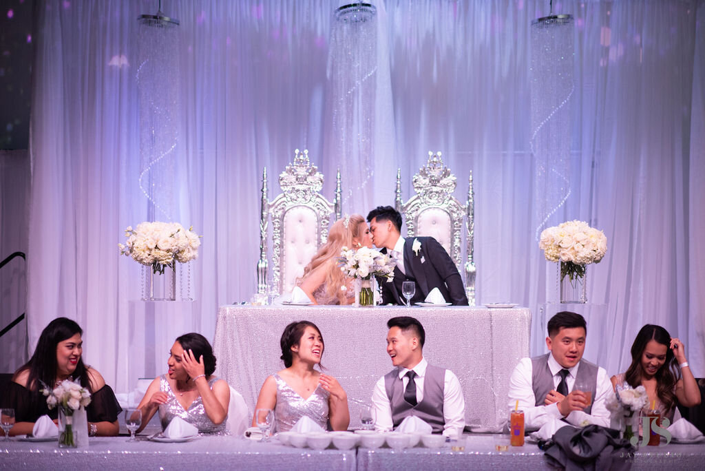 Bride and groom sit with their wedding party with an all white design  at their reception.