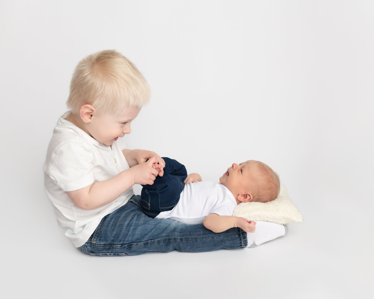 Heartwarming moment of a toddler meeting his newborn sibling, photographed on a clean white background in studio by Meraki Photographic Creations. Captured in-studio at Meraki Photographic Creations in Paris, Ontario.