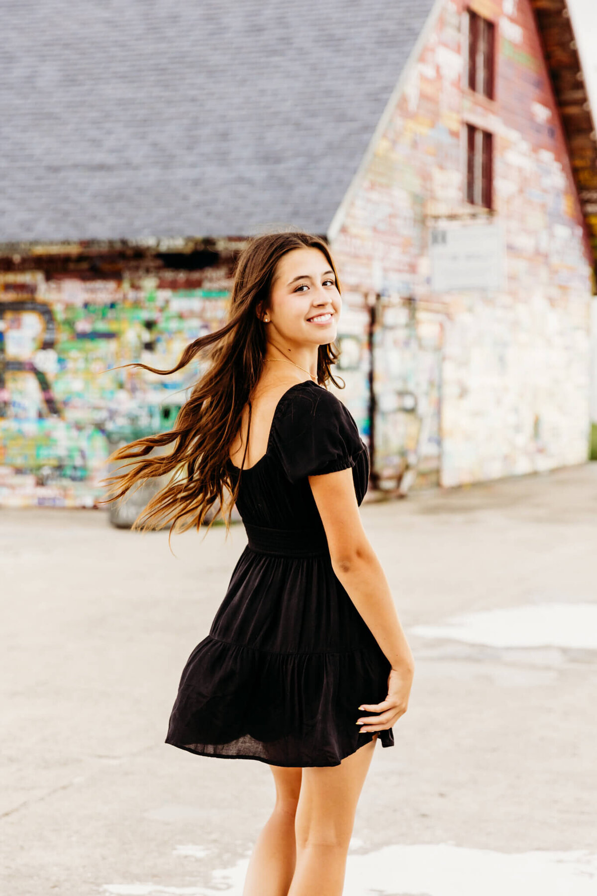 pretty teenage girl in a short black dress, flipping her hair and looking back by Ashley Kalbus Photography