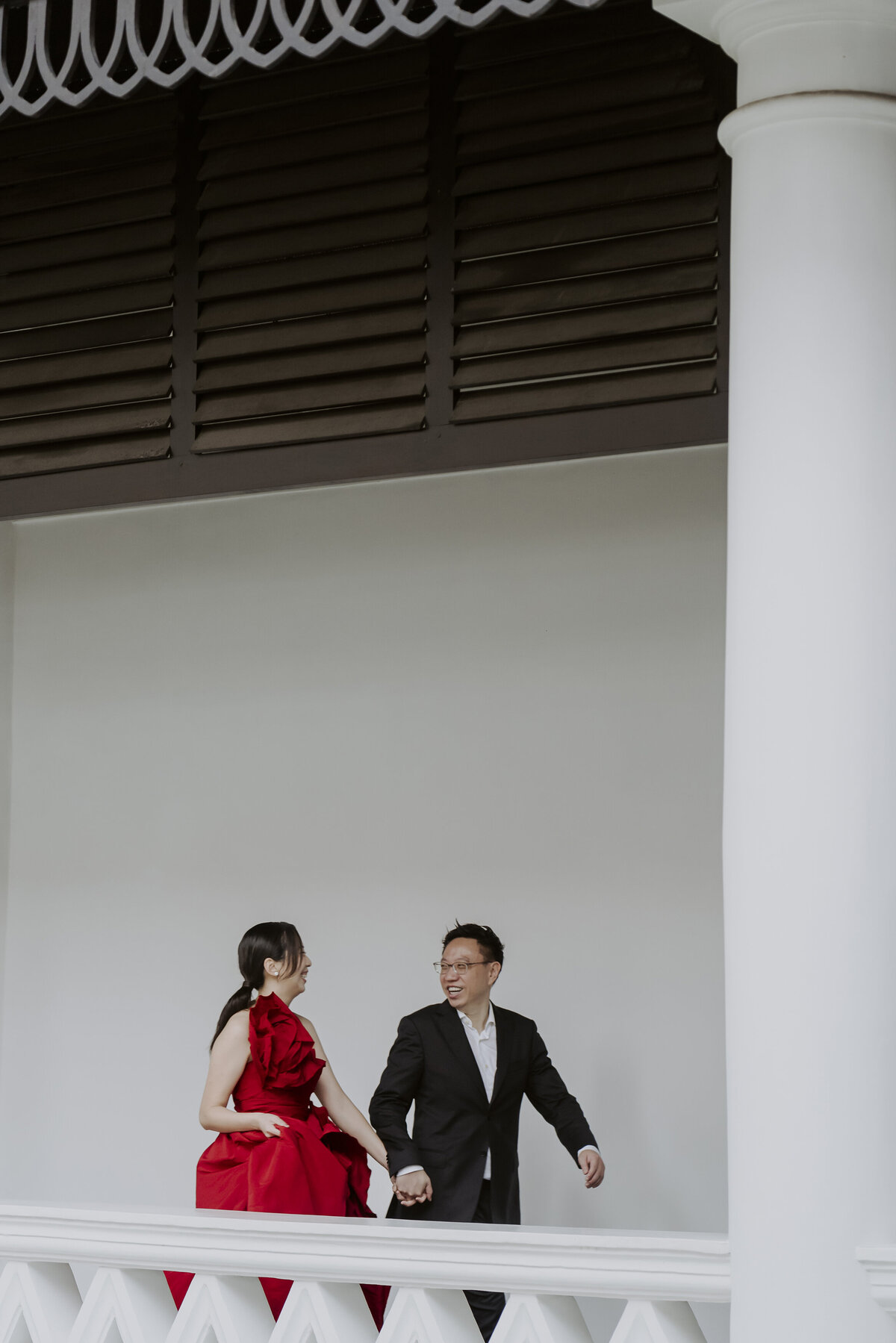 the bide and groom walking hand in hand on the balcony of the raffles hotel