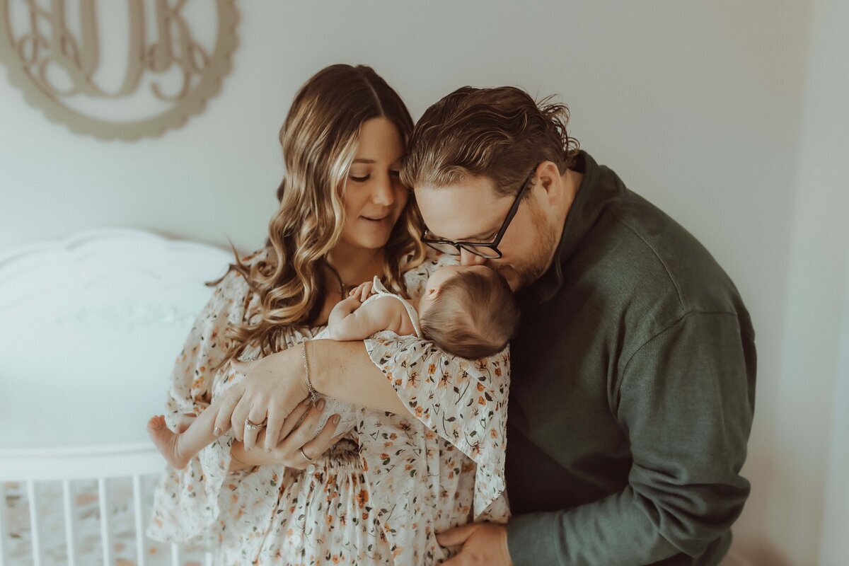 In a cozy nursery adorned with charming decor, a couple stands closely, tenderly cradling their baby. This intimate scene beautifully captures the essence of Macon newborn photography.
