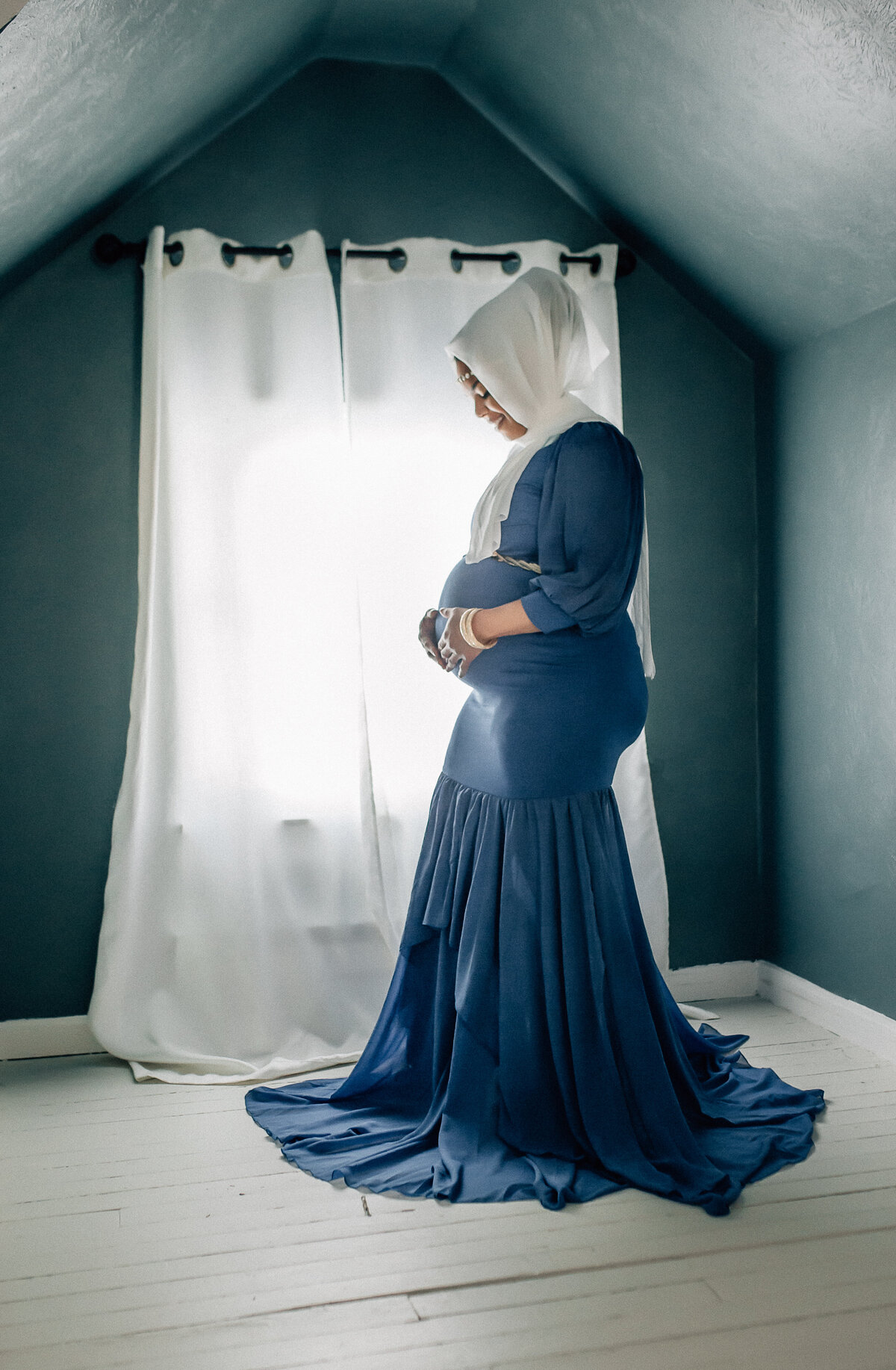 Maternity photograph of mom standing next to window holding belly.