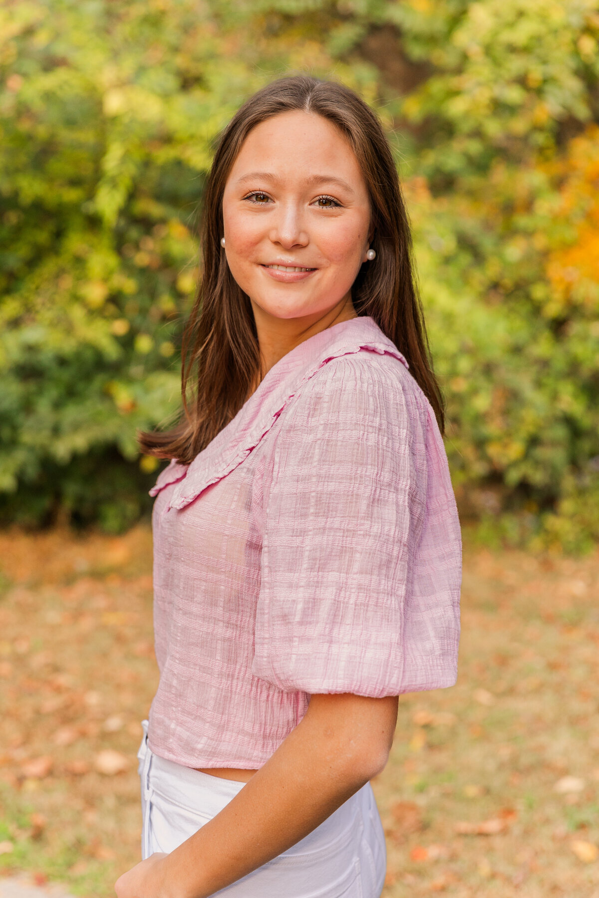 senior girl wearing a pink blouse looking at the camera over her shoulder in a Buckhead park during photo session