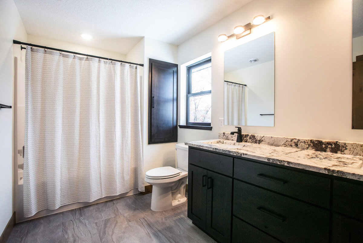 Custom bathroom with dark cabinets, shower and modern accents in Elk River home by Cornerstone Custom Builds