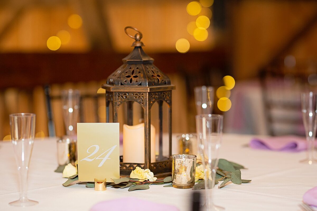 Wedding table centerpieces including a metal lantern, votive candles, and greenery