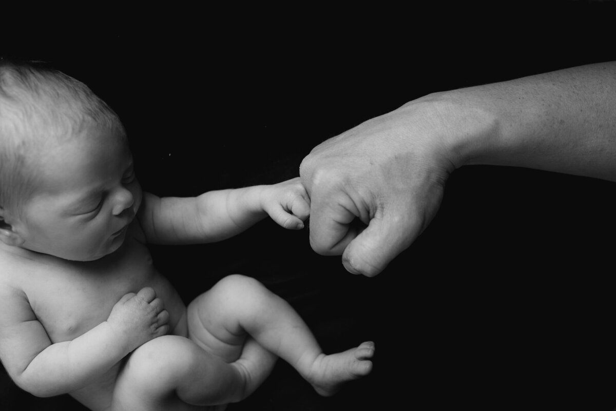 Heartwarming newborn portrait capturing a baby fist-bumping with a parent's hand, symbolizing connection and love. Captured in Overland Park, Kansas, for families seeking intimate and meaningful newborn photography in the Kansas City metro area.