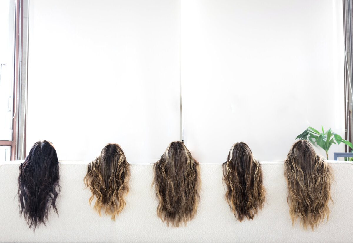 Three hair extensions models are standing together and smiling while holding hand-tied wefts and a color swatch ring.