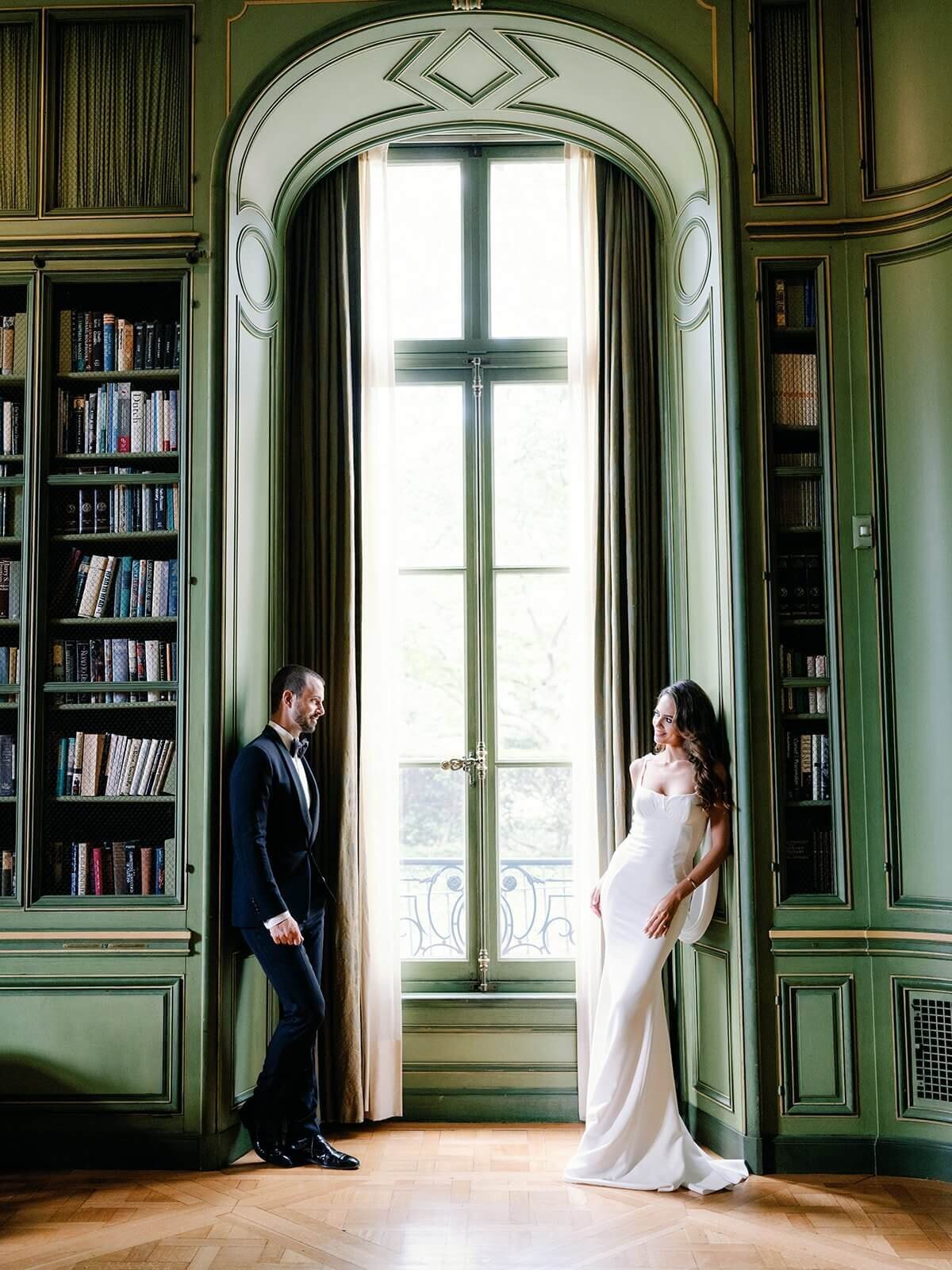 Couple stands opposite side of floor length windows in the library  at Meridian House in DC