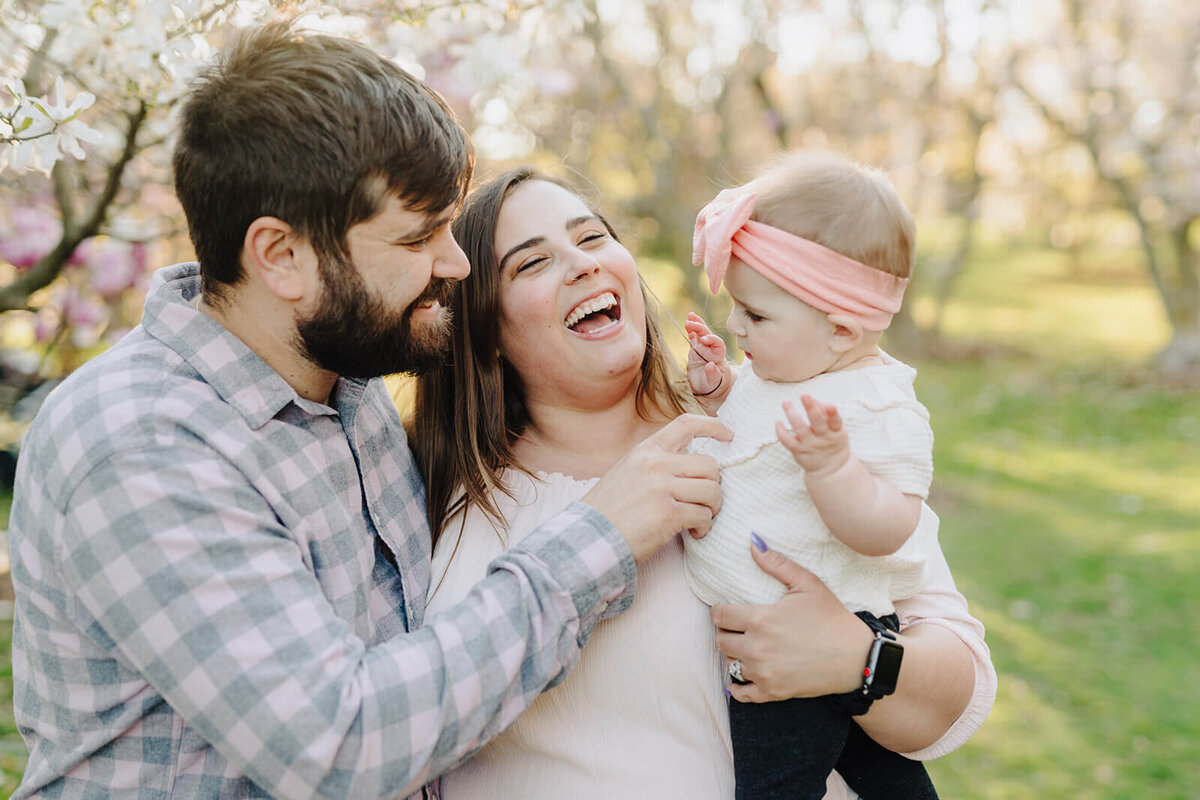 couple holding a baby standing in front of cherry blossom tree