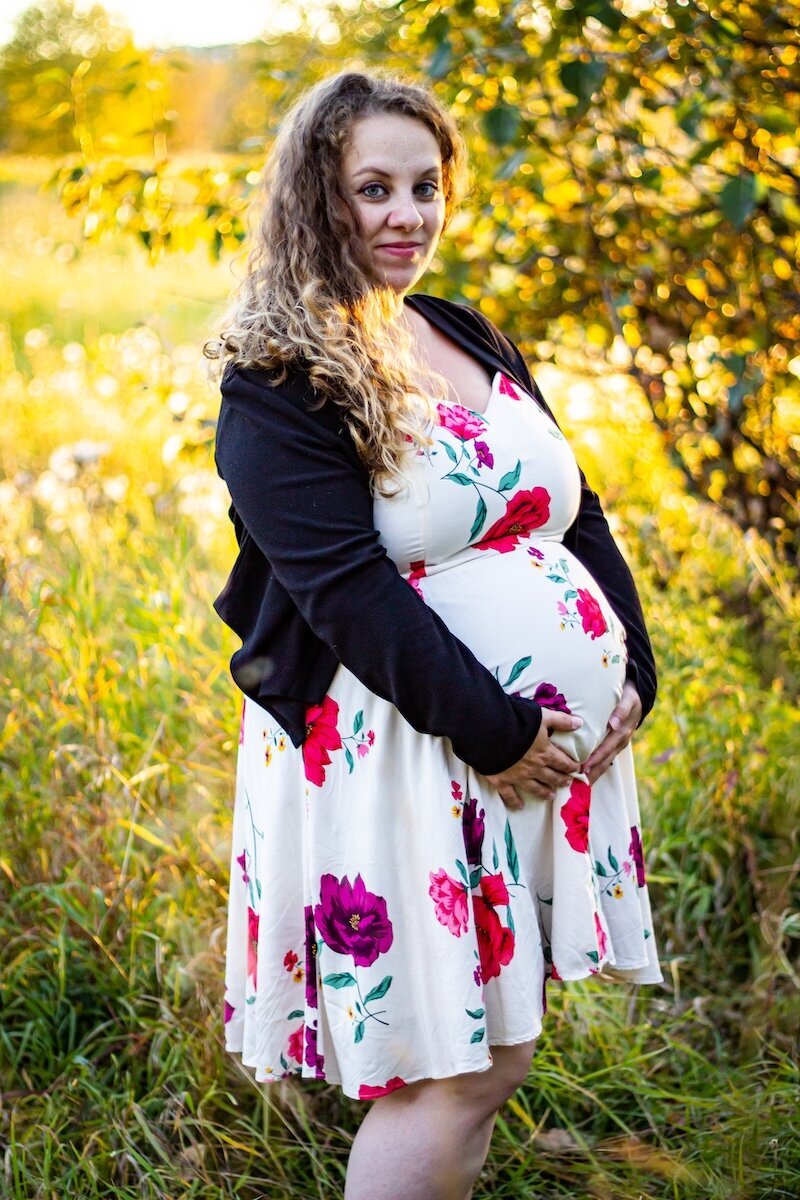 a pregnant woman wearing a white floral dress holding her belly