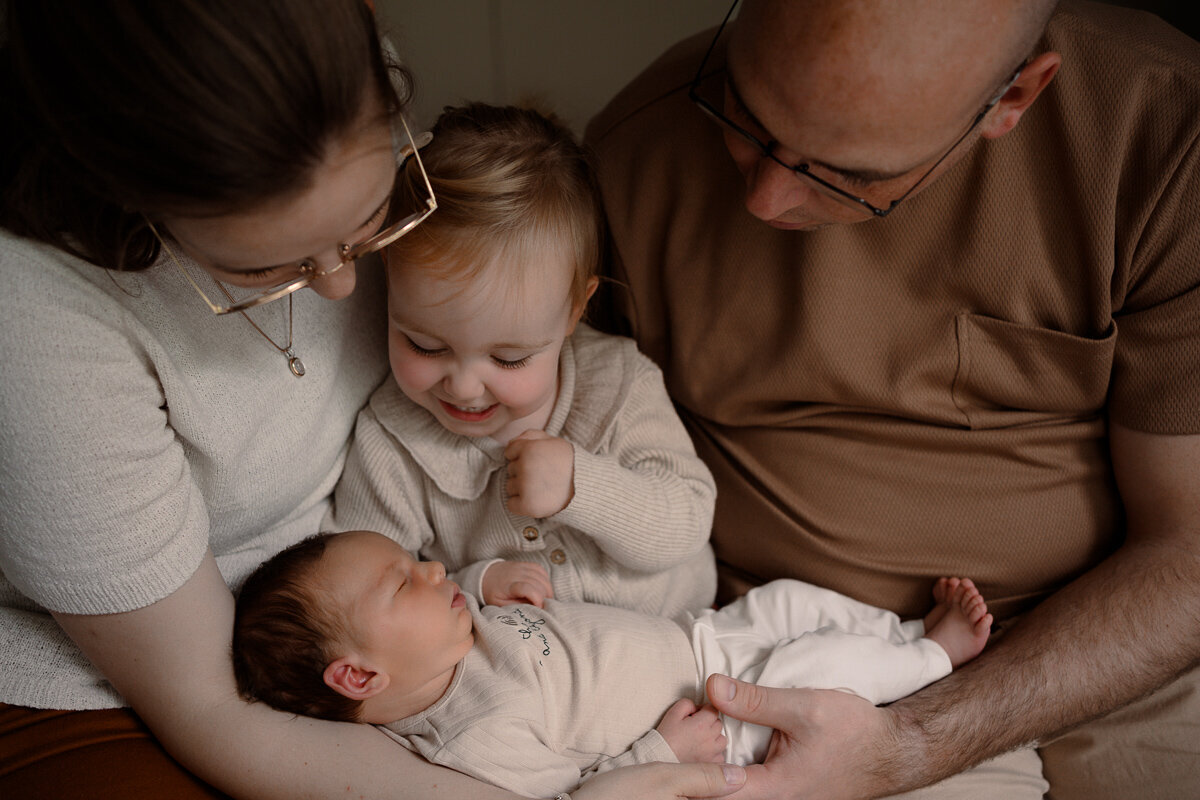 Zus kijkt lachend naar haar broertje terwijl ze bij moeder op schoot zit